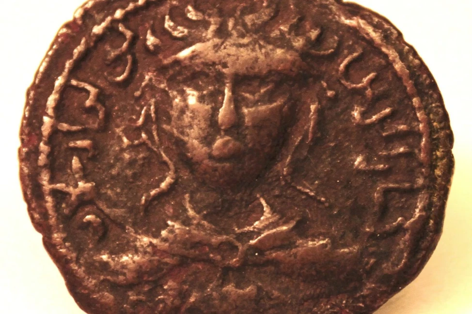 Древняя бронзовая монета с профилем правителя. На поверхности видны следы времени, потёртости и надписи по краю монеты.
