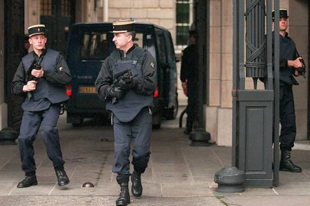 Французские полицейские в форме с оружием охраняют фургон у ворот здания в Париже, 1995