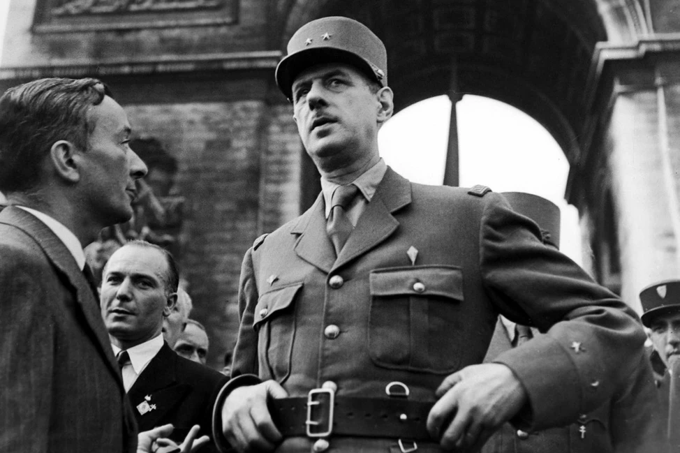 Офицер в военной форме и фуражке среди людей на фоне арочного сооружения, историческое чёрно-белое фото.