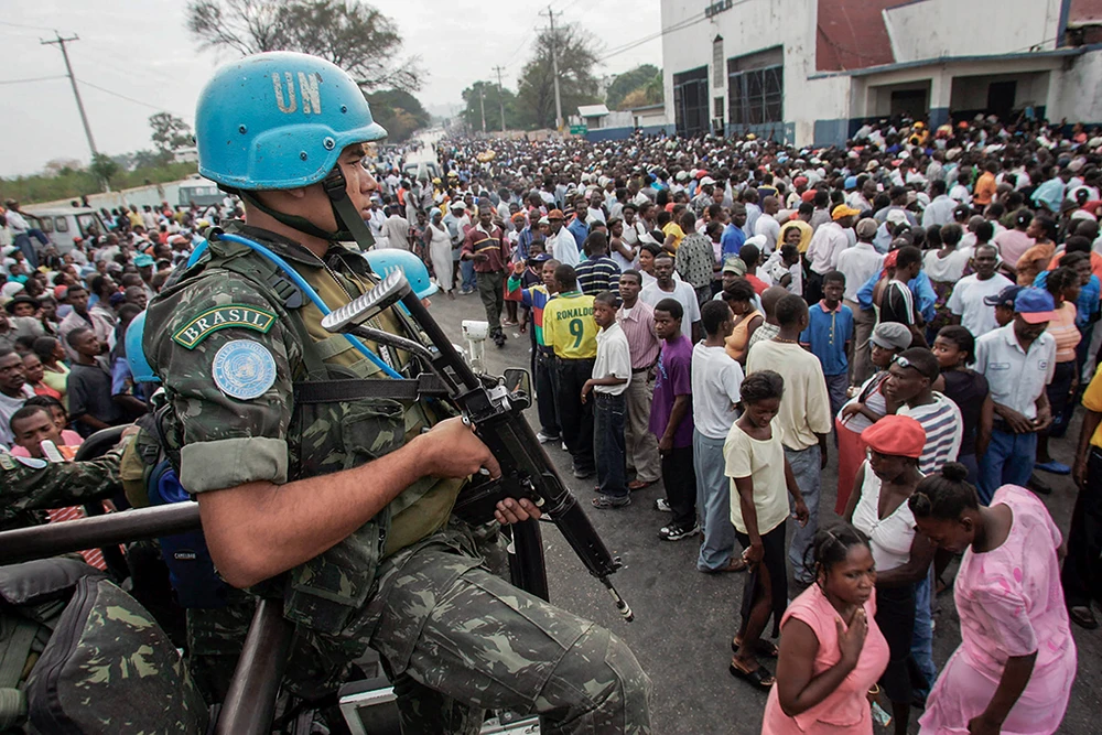 Миротворец ООН из Бразилии в голубом шлеме с оружием среди большой толпы гражданских