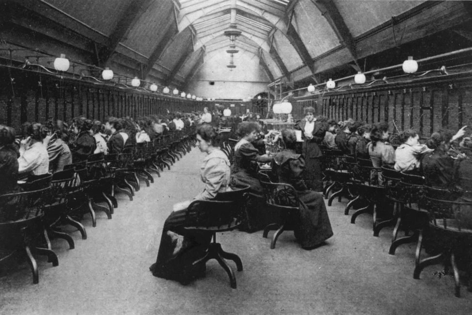 Просторный зал телефонной станции с арочным потолком: ряды коммутаторов вдоль стен, женщины-операторы за работой