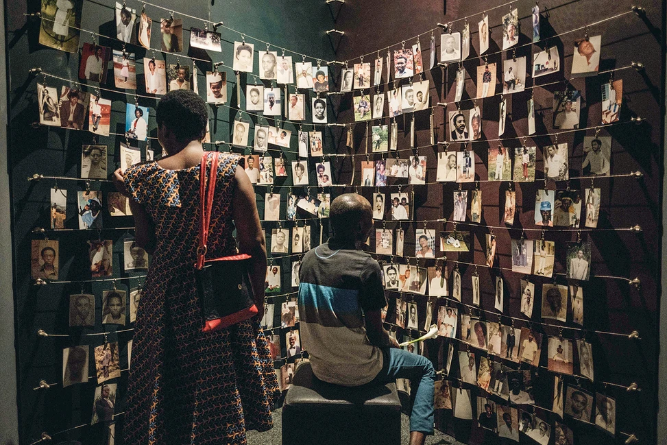 Посетители рассматривают фотопортреты, развешанные на шнурах в несколько рядов на стене в мемориальном зале