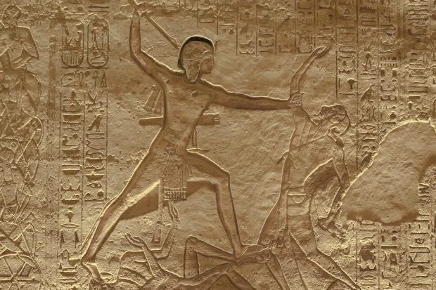 Древнеегипетский рельеф: фараон в характерной позе с поднятой рукой поражает врага. Вокруг — иероглифические надписи.