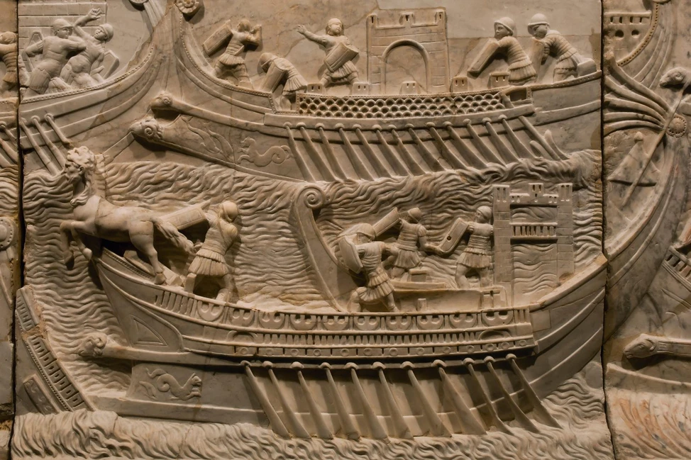 Древнеримский рельеф: корабли с гребцами, воины, лошадь на палубе, волны, крепостные стены.