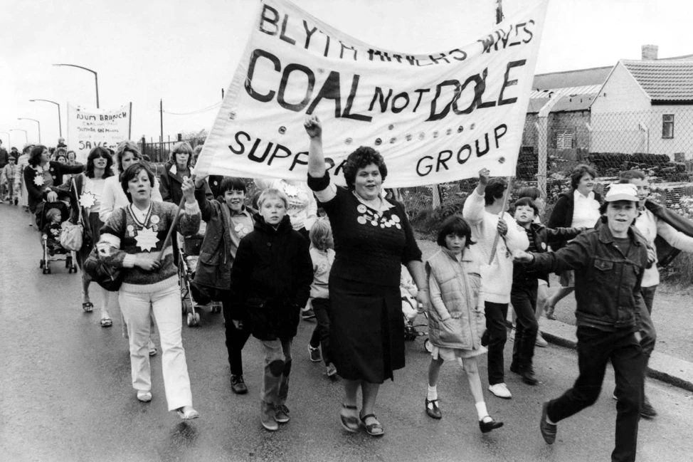 Участники уличного марша несут большой транспарант Coal Not Dole Support Group, впереди идут женщины и дети