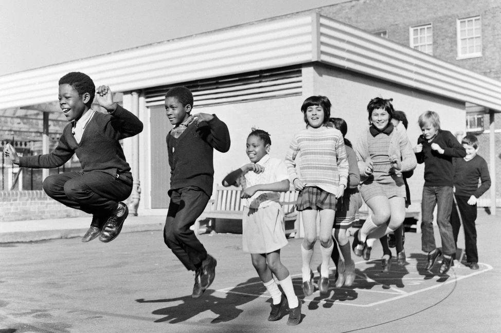 Школьники прыгают по разметке на школьном дворе у здания младшей школы