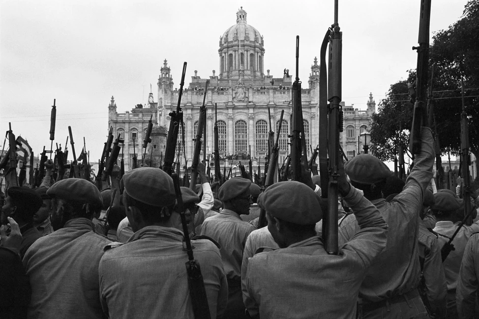 Солдаты в беретах с поднятыми винтовками на фоне здания с куполом в Гаване, 1961 год