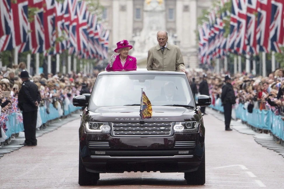 Елизавета II и принц Филипп едут в открытом Range Rover по улице с флагами и толпой зрителей
