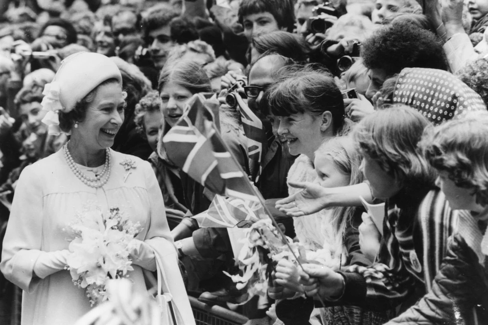 Елизавета II улыбается детям с британскими флагами за ограждением