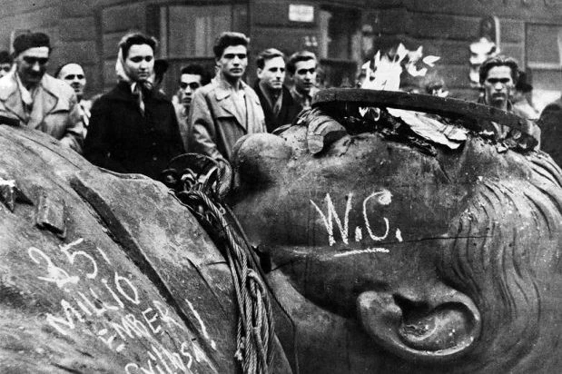 Голова разрушенной статуи Сталина с граффити лежит на земле, вокруг стоят молодые люди, Будапешт, 1956 год