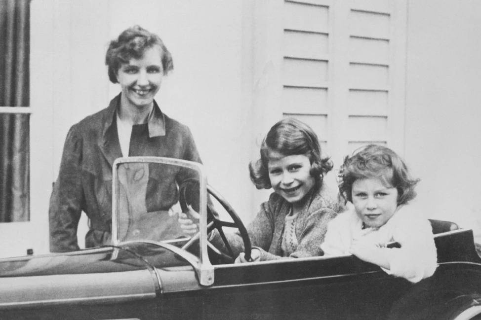 Юные Елизавета и Маргарет сидят в детском автомобиле рядом с гувернанткой, чёрно-белый снимок