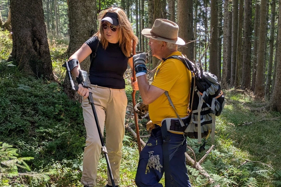 Женщина с металлоискателем и мужчина с рюкзаком разговаривают в лесу