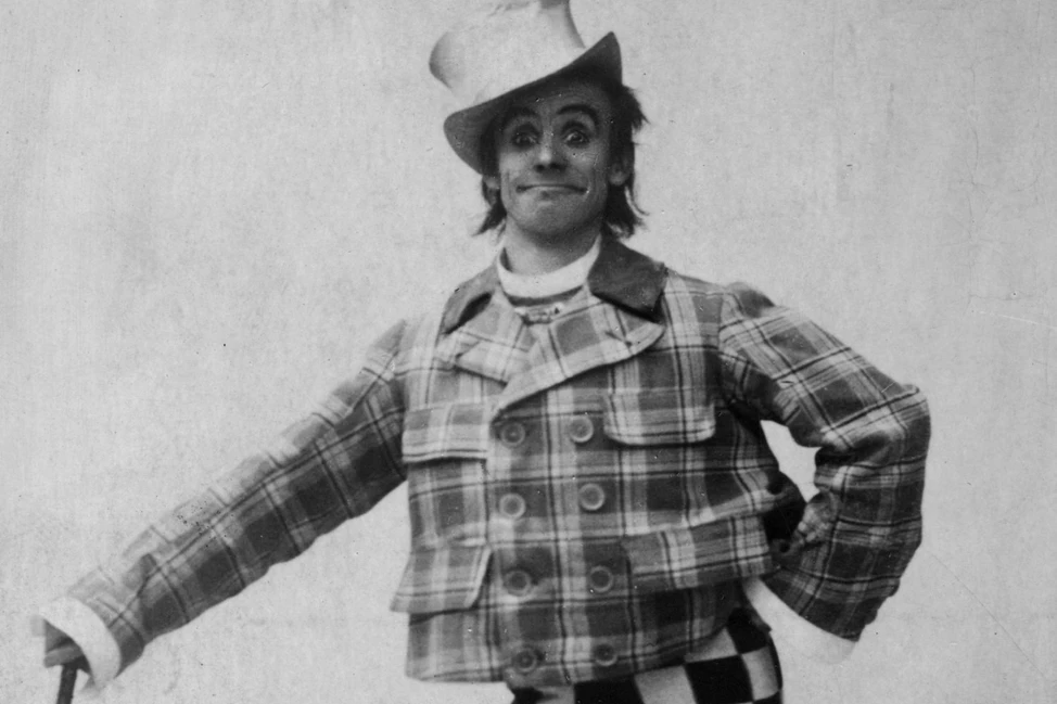 Alt-текст: Комик в клетчатом костюме и цилиндре с театральным гримом, чёрно-белое фото 1890-х годов