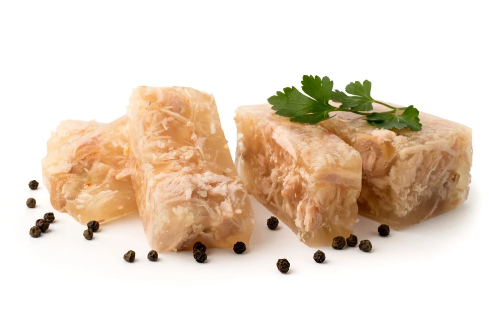 Куски куриного заливного с петрушкой и горошинами чёрного перца на белом фоне